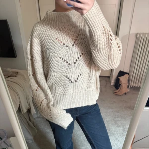 Beige stickad tröja från Lindex - Säljer en mysig beige stickad tröja från Lindex med ett snyggt hålmönster. Tröjan har långa ärmar och en hög krage som ger extra värme. Perfekt för kyliga dagar!