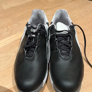 Svarta golfskor från Adidas - Säljer ett par svarta golfskorfrån Adidas med vita detaljer och snörning. Skorna är oanvända.