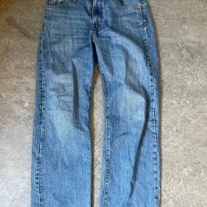 Blå jeans från Levis - Säljer ett par klassiska blå Levis jeans med rak passform. De har en traditionell femficksdesign och en knappgylf. Perfekta för en avslappnad stil. Ett litet hål tillkommer.