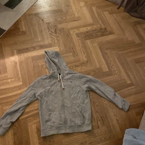 Grå hoodie med dragkedja från Morris - Säljer en grå hoodie med dragkedja och huva från Morris. Tröjan har långa ärmar och en praktisk ficka framtill. Perfekt för en avslappnad stil.