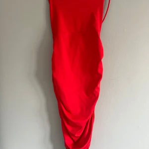 Röd klänning från BikBok - Snygg röd klänning från BikBok med snörning i ryggen och draperad detalj på sidan. Perfekt för en kväll ute eller en speciell tillställning. Klänningen har en tight passform och är axelbandslös.