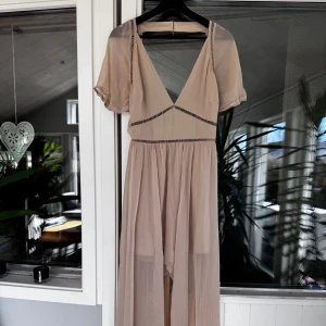 Beige klänning med volangdetaljer - Beige klänning med v-ringning och öppen rygg med prislapp på. Väldigt luftig och söt men var inte rätt storlek för mig. Rensar ur min garderob från en hel del kläder🌼 Om du ser något mer i min profil som du gillar så skickar jag med det till dig också!😊 Fler kläder kommer! 