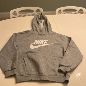 Grå hoodie från Nike - Säljer en klassisk grå hoodie från Nike med stor vit logga på framsidan. Tröjan har en bekväm passform med långa ärmar och en praktisk magficka. Perfekt för en avslappnad stil. 🩶