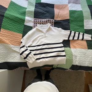 Vit och svart randig tröja från Lindex - Säljer en stilren vit tröja från Lindex med svarta ränder och dragkedja vid halsen. Perfekt för en avslappnad stil. Tröjan har långa ärmar och är tillverkad i ett mjukt material.