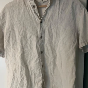 Beige kortärmad skjorta från H&M - Säljer en stilren beige kortärmad skjorta från H&M. Skjortan har en avslappnad passform med knappar framtill och är tillverkad i ett lätt och luftigt material, perfekt för varma dagar. Pris kan diskuteras!