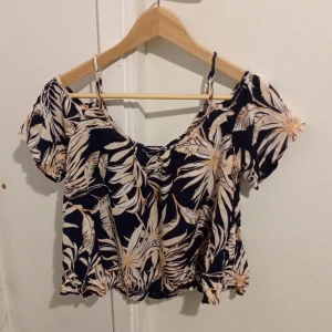 Blommig topp från Vero Moda - Säljer en snygg blommig topp från Vero Moda. Den har en mörkblå bas med ljusa blommönster och korta ärmar. Toppen är croppad och har en luftig passform med smala axelband. Skriv gärna om du vill ha mer information om toppen 