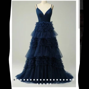 Marinblå balklänning med volanger - Elegant marinblå balklänning med spagettiband och flera lager av volanger. Klänningen har en v-ringad urringning och är perfekt för en glamorös kväll. Den långa designen ger en sofistikerad look. Den är aldrig använd och pris kan diskuteras vid snabbt köp