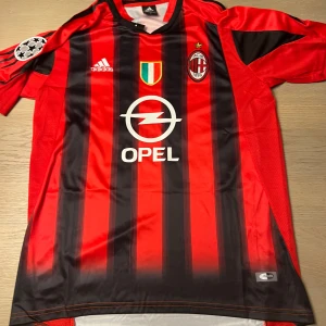 Röd och svart randig fotbollströja från Adidas - Säljer en klassisk röd och svart randig fotbollströja från Adidas med korta ärmar. Tröjan har tryck på framsidan och baksidan, inklusive ett stort nummer och namn. Perfekt för fotbollsfans som vill visa sitt stöd.