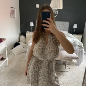 Beige mönstrad klänning från Mango - Säljer en snygg beige klänning från Mango med leopardmönster. Klänningen har en luftig passform och är ärmlös med knytning i halsen. Perfekt för en stilren look! Öppen i ryggen 