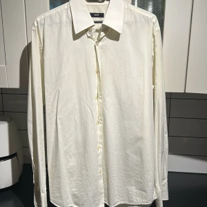 Vit skjorta från BOSS - Säljer en stilren vit skjorta från BOSS med klassisk krage och knappar framtill. Skjortan har långa ärmar och är perfekt för en elegant look. Passar utmärkt till både formella och avslappnade tillfällen.