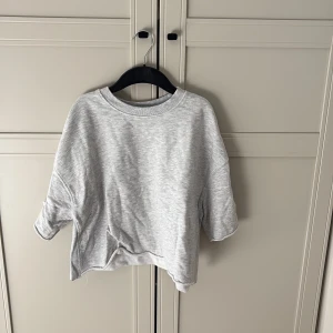 Grå tröja från Zara - Säljer en stilren grå tröja från Zara med trekvartsärm och rund hals. Perfekt för våren. Tröjan har en lös passform och är tillverkad i ett mjukt material.