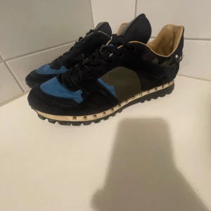 Valentino rockrunners - Snygga sneakers från Valentino i en mix av blått, svart och grönt. Skorna har coola nitar runt sulan och en unik design. Perfekta för dig som vill sticka ut med stil. 