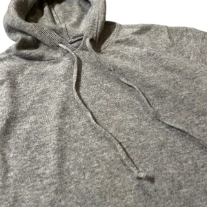 Merino Ull hoodie - Säljer en stilren grå stickad hoodie med justerbar huva och ribbade muddar. Perfekt för kyliga dagar och en avslappnad look. Passar både till jeans och mjukisbyxor.