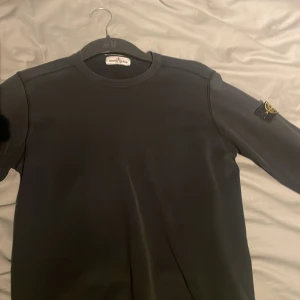 Svart långärmad tröja från Stone Island - Säljer en stilren svart långärmad tröja från Stone Island. Tröjan har en rund halsringning och det ikoniska Stone Island-märket på ärmen. Perfekt för en casual look.
