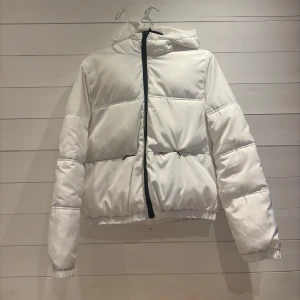 Vit pufferjacka från H&M - Säljer en snygg vit pufferjacka från H&M med dragkedja framtill. Jackan har en huva och långa ärmar, perfekt för kyligare dagar. Den är både stilren och praktisk, vilket gör den till ett måste i garderoben. Passar perfekt för vår och höst!