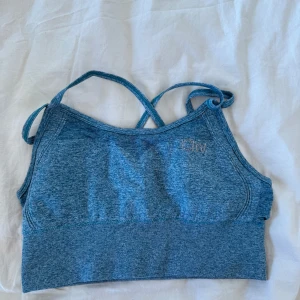  sporttopp Iciw  - Säljer en blå sporttopp med korsade axelband och brottarrygg. Perfekt för träning och ger bra stöd. Toppen har en stilren design med en liten logga framtill.
