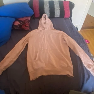 Rosa hoodie med broderad text - Säljer en beige hoodie med broderad text 'in the heat of the moment' på framsidan. Tröjan har en klassisk design med huva och långa ärmar. Perfekt för en avslappnad stil.