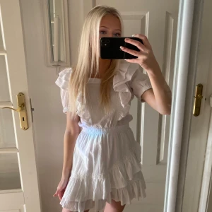 Vit klänning med volanger - Säljer en söt vit klänning med volanger och korta ärmar. Perfekt till studenten 🥰 Klänningen har en knytning i ryggen och en luftig passform. 