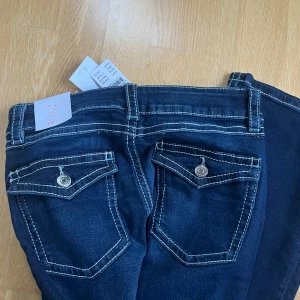 Mörkblå jeans med vita sömmar - Snygga mörkblå jeans från gina tricot Young med kontrasterande vita sömmar. De har en klassisk femficksdesign och dekorativa knappar på bakfickorna. Perfekta för en stilren look.