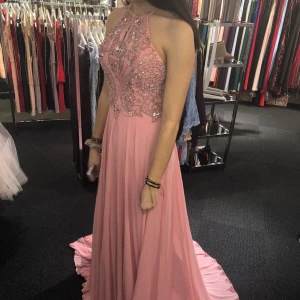 Rosa långklänning med pärlor - Elegant rosa långklänning med detaljerade pärlor och broderier på livet. Klänningen har en öppen rygg med smala axelband som kan korsas. Använd endast en kväll, köpt för 1500kr men säljs för 500kr