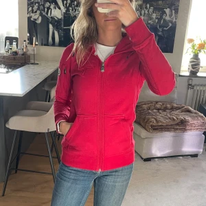 Röd hoodie från Pelle P - Säljer en snygg röd hoodie från Pelle P med dragkedja och huva. Hoodie har en broderad logga på bröstet. Den har en normal passform och långa ärmar. Nypris 1400kr