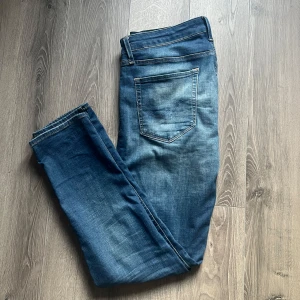 Blåa jeans från Jack&Jones - Snygga blå jeansbyxor med en klassisk femficksdesign och lätt slitna detaljer. Byxorna har en rak passform och är perfekta för en avslappnad stil. De har en knappgylf och en läderpatch på baksidan av midjan.