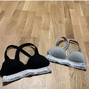 Calvin Klein bh i svart och grått - Två Calvin Klein bh:ar i svart och grått med märkets logga på det elastiska bandet. Perfekta för en bekväm och stilren look.