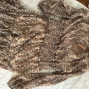 Leopardmönstrad miniklänning från Zara - Snygg leopardmönstrad klänning från Zara med smockdetaljer i midjan. Klänningen har långa ärmar och en knytning vid halsen. Perfekt för en trendig sommarlook! Passar s-m. Använd en gång. 