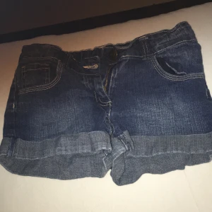 Blå jeansshorts med uppvikta ben - Säljer ett par snygga blå jeansshorts med uppvikta ben och klassisk femficksdesign. Shortsen har en dragkedja och knapp framtill. Perfekta för en avslappnad stil.
