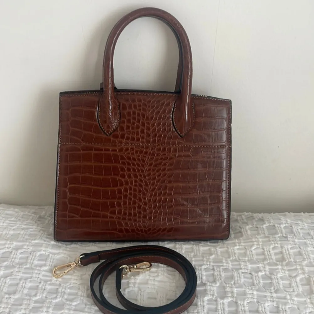 Elegant brun handväska i krokodilpräglat skinn. Väskan har två handtag och en avtagbar axelrem med guldfärgade detaljer. Den har en dragkedja upptill och en stilren design som passar perfekt för en chic look.. Laukut & Käsilaukut.