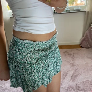 Mönstrad kjol - Säljer en söt grön blommig kortkjol med volangdetaljer. Perfekt för varma dagar och ger en fräsch look. Kjolen har en bekväm passform och är lätt att matcha med olika toppar.Kjolen har inbyggda shorts!