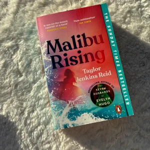 Malibu Rising - Boken 'Malibu Rising' av Taylor Jenkins Reid är en Sunday Times bestseller. Omslaget har en färgglad design med en bild av en person i vågorna. Perfekt för strandläsning och fans av författarens tidigare verk som 'The Seven Husbands of Evelyn Hugo'.