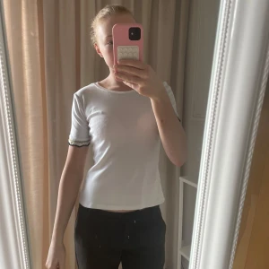 Vit kortärmad topp med spetsdetaljer - Säljer en vit kortärmad topp med fina spetsdetaljer vid ärmsluten. Toppen har en rund halsringning och en bekväm passform. Perfekt för en stilren look.