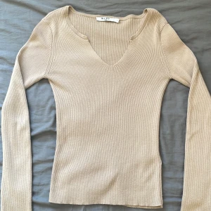 Beige ribbad tröja från NA-KD - Säljer en stilren beige ribbad tröja från NA-KD. Tröjan har en v-ringad hals och långa ärmar, perfekt för en chic och bekväm look. Passar utmärkt till både jeans och kjol.