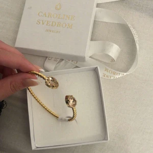 Armband från Caroline Svedbom - Jag säljer mitt Caroline svedbom armband eftersom jag inte använder de längre. Säljer det till ett billigare pris eftersom färgen e lite sliten men annars är den i bra skick. Guld med rosa stenar.