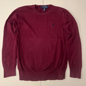 Vinröd tröja från Ralph Lauren - Säljer en stilren vinröd tröja från Ralph Lauren med rund hals och broderad logga på bröstet. Tröjan har långa ärmar och ribbade muddar vid ärmslut och nederkant. Perfekt för en klassisk look. Storlek Ca 152.