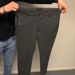 Grå kostymbyxor från Gabba - Snygga grå kostymbyxor från Gabba i storlek L. Byxorna har en klassisk design med knappar och dragkedja framtill. Perfekta för en stilren look.