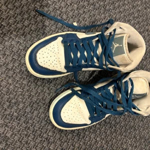 Nike Air Jordans i blått och vitt - Snygga Nike Air Jordans i en fräsch kombination av blått och vitt. Skorna har en klassisk design med snörning och perforerade detaljer på tån för extra ventilation. Perfekta för både stil och komfort.