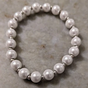 Vitt pärlarmband - Elegant vitt pärlarmband med silverfärgade detaljer. Perfekt för att ge en klassisk touch till din outfit. Armbandet är elastiskt och passar de flesta handleder.
