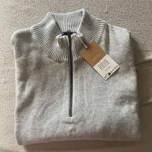 Grå tröja med dragkedja från LMTD - Säljer en stilren grå tröja från LMTD med halv dragkedja och ribbad krage. Perfekt för kyligare dagar med sin mjuka och bekväma passform. Tröjan har långa ärmar och ribbade muddar vid ärmslut och nederkant.