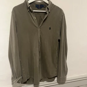 Grå skjorta från Ralph Lauren - Säljer en stilren grå skjorta från Ralph Lauren. Skjortan har långa ärmar och knappar framtill. Den är tillverkad i ett lätt och bekvämt material, perfekt för både vardag och mer uppklädda tillfällen. Klassisk design med broderad logotyp på bröstet. Designen är Featherweight Mesh.