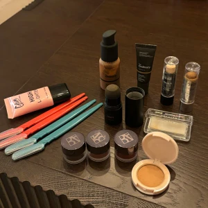 Sminkset med foundation, highlighter och mer - Ett komplett sminkset med foundation från The Ordinary, highlighter i rosa tub, concealer sticks, och flera ögonskuggor i burkar. Inkluderar även en kompakt puder och sminkborstar i olika färger.