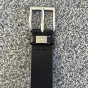 Svart skärp från Boss - Snyggt svart skärp från Boss med ett stilrent silverfärgat spänne. Skärpet är tillverkat i skinn och har en klassisk design som passar till många olika outfits. Kan gå ner vid snabb affär 🕰️