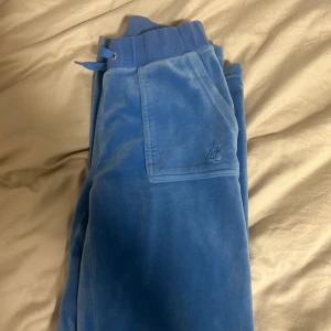 Blå mjukisbyxor från Juicy Couture - Säljer ett par mjuka och bekväma blå mjukisbyxor från Juicy Couture. Byxorna har en elastisk midja med snörning och praktiska fickor framtill. Perfekta för en avslappnad stil.
