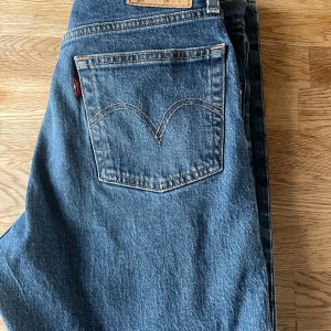 Levi's blå jeans - Klassiska blå Levi's 501 jeans med knappgylf. De har en traditionell passform och är perfekta för en avslappnad stil. Märkeslappen syns tydligt på baksidan. Innerbens längden är 62