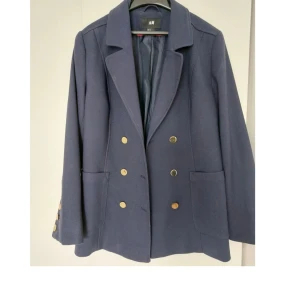 H&M Navy kavaj med guldknappar - Kavaj/blazer. Mycket gott skick, sparsamt använd. Mörkblå med guldknappar fram och på ärmarna. Fickor på sidan. Snygg passform. 