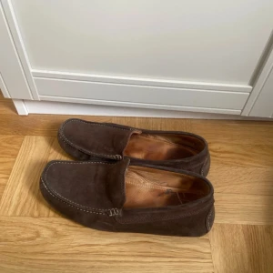 Bruna mocka loafers från Gant - Säljer ett par bruna loafers i mocka från Gant. Skorna har klassisk design med rund tå, synliga sömmar och diskret logga bak. Perfekta för en stilren och avslappnad look.