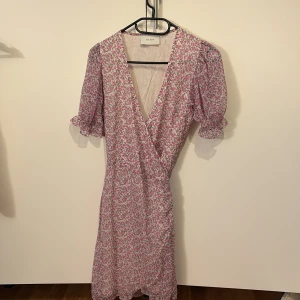 Blommig omlottklänning från Neo Noir - Söt kort blommig klänning från Neo noir med puffärmar och omlottmodell. Klänningen har v-ringning och volangdetaljer vid ärmslut. Perfekt för vår och sommar!❤️❤️storlek xs-s❤️
