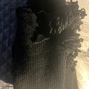 Svart stickad tröja med fransdetaljer från Luisa Cerano - Säljer en svart stickad tröja från Luisa Cerano med unika fransdetaljer vid halsringning, ärmslut och på magen. Tröjan har lång ärm och en cool, chunky känsla som sticker ut. Perfekt för dig som vill ha något annorlunda i garderoben.