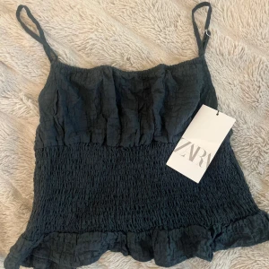 Mörk blå linnetopp från Zara - Supersöt mörkt blått linnetopp från Zara med smockad midja och volangkant nertill. Tunna axelband och lätt skrynkligt tyg ger en avslappnad men trendig look. Perfekt att matcha med jeans eller kjol. Det är storlek L men hade kunnat vara S, den är liten 
